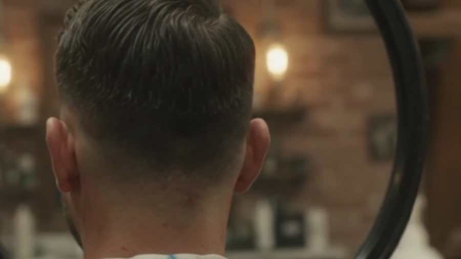 Back of a client's head showing a clean tapered fade in a hand mirror